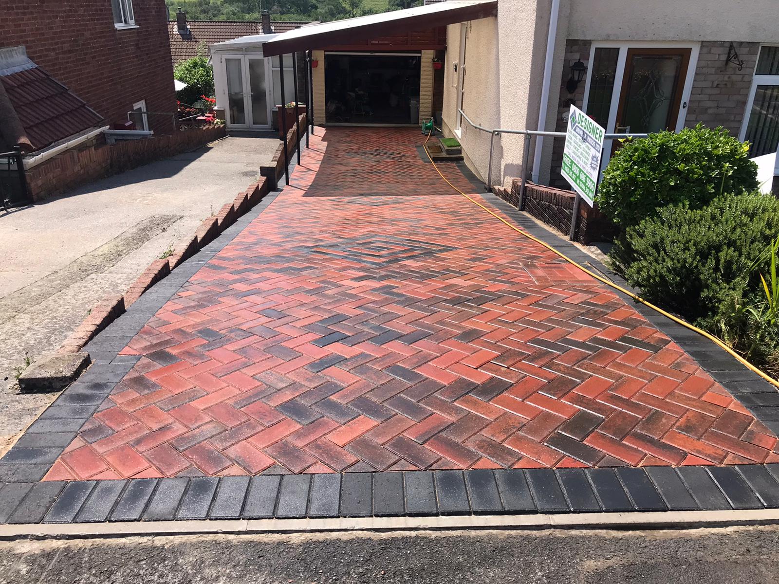 Sloped red herringbone block driveway with a diamond motif and carport in Cardiff